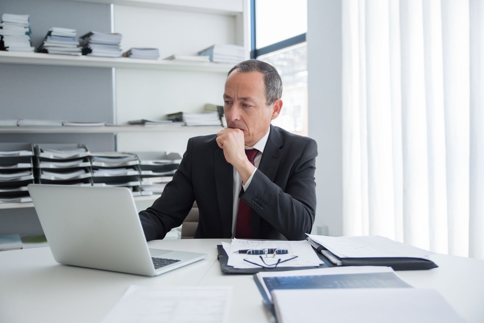 Dirigeant de PME réfléchissant à son bureau, documents et ordinateur portable